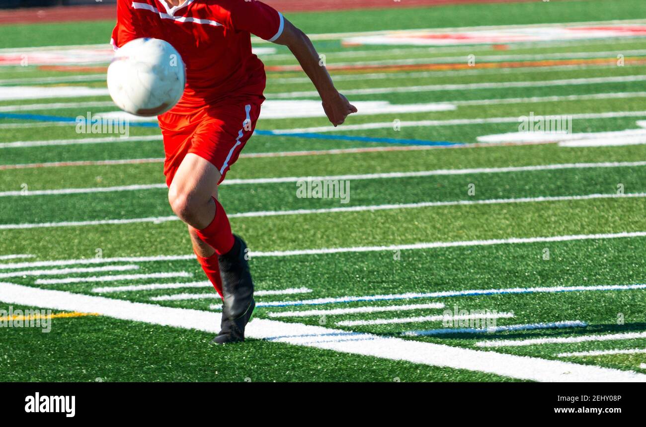 Accent sélectif sur un joueur de football d'école secondaire dans un uniforme rouge chassant une balle rebondissante pendant un match Banque D'Images