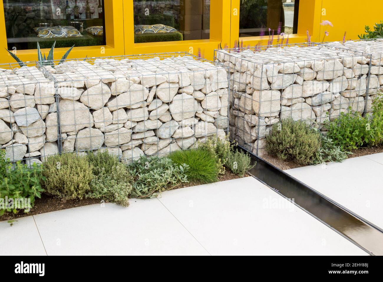 jardin avec un mur de gabions rempli de pierre un jardin rill eau dispose d'une terrasse pavée - plantation d'herbes méditerranéennes frontières plantes Royaume-Uni Banque D'Images