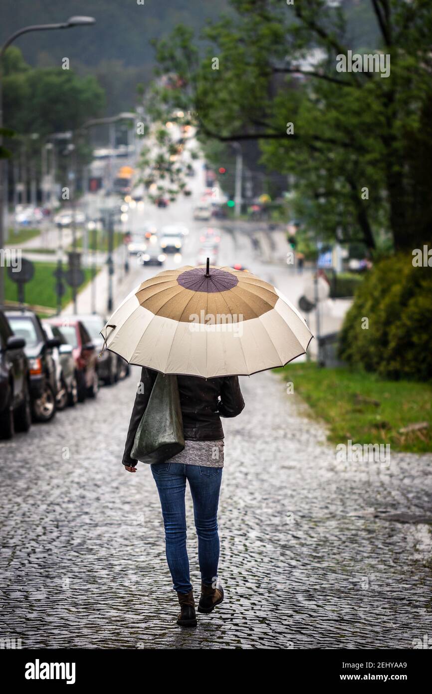 Femme avec parapluie marchant sur la route en ville sous la pluie. Femme tendance portant des vêtements décontractés de style urbain. Vie urbaine Banque D'Images
