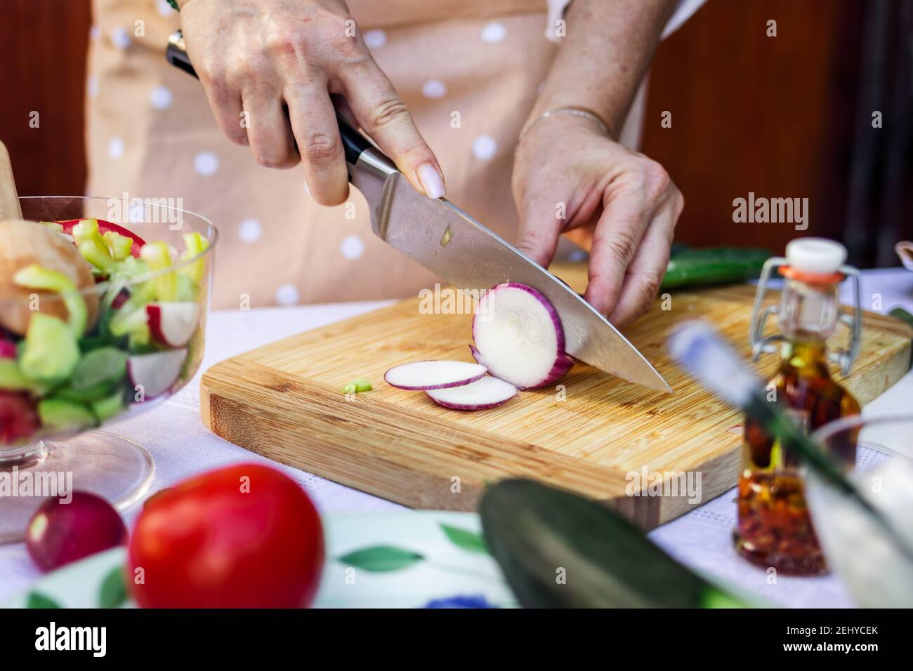 Femme coupant l'oignon rouge avec un couteau de cuisine sur une planche en bois. Préparation des aliments. Légumes en gros plan à la main Banque D'Images