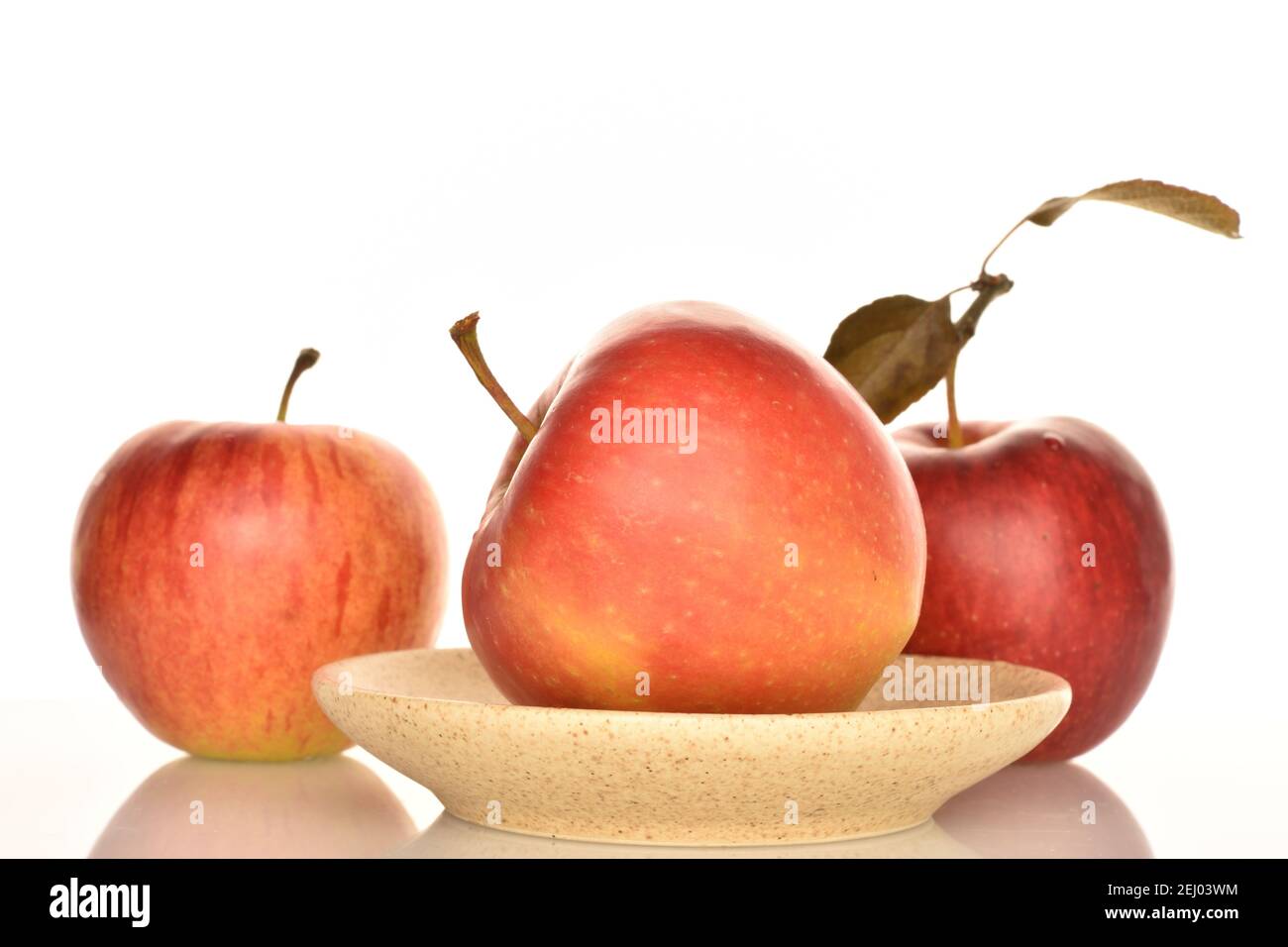 Une pomme délicieuse biologique mûre rouge entière se trouve sur une soucoupe en céramique, deux autres sont en arrière-plan. L'arrière-plan est blanc. Banque D'Images