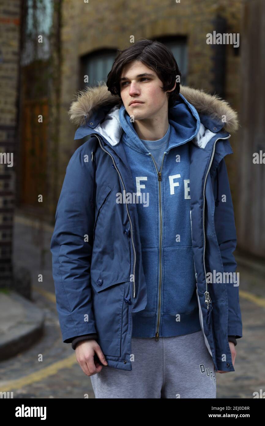 Jeune homme en vêtements de sport décontractés et manteau d'hiver. Portrait sur toute la longueur du corps avec un arrière-plan urbain. Banque D'Images