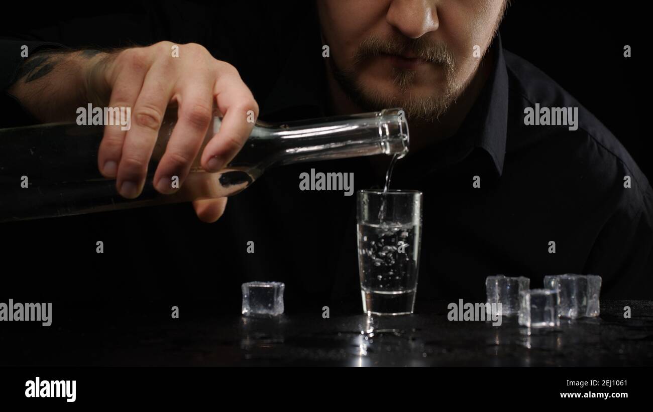Un alcoolique qui déverse de la vodka surgelée de la bouteille dans un  verre à bière avec des glaçons sur fond noir. Homme buvant de l'alcool froid  et transparent buvez du saké,