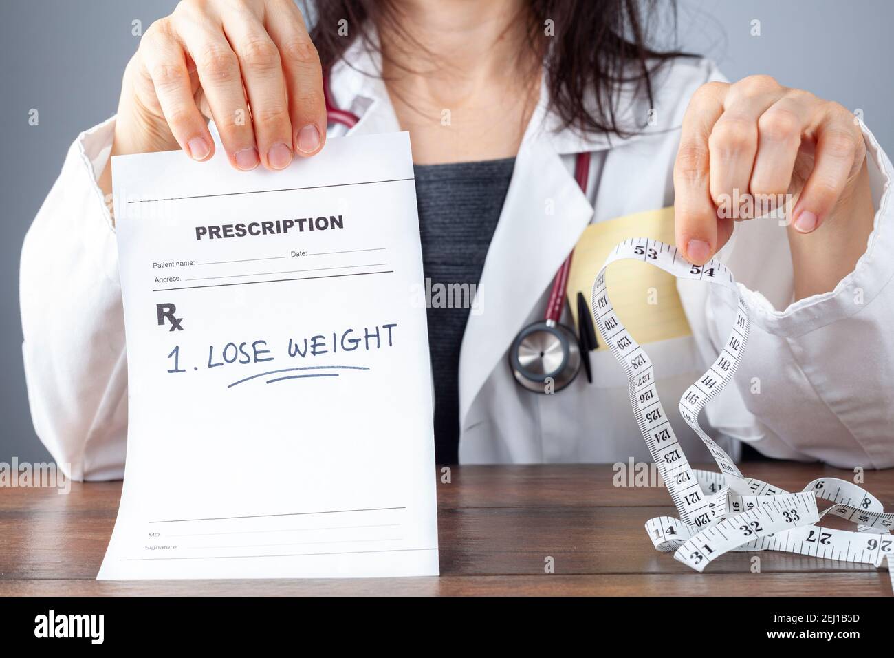 Une femme médecin tient une ordonnance qui dit perdre poids dans une main et un mètre ruban pour l'abdomen mesure de circonférence sur l'autre Banque D'Images