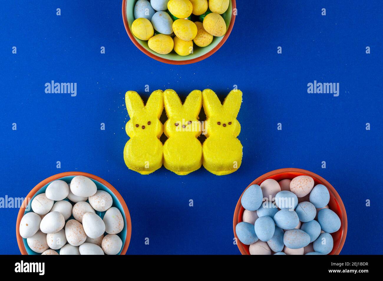 Trois petits lapins de pâques en guimauves verglacées jaunes avec trois petits bols remplis d'œufs de chocolat enrobés de sucre croustillant pour pâques. Un appareil polyvalent Banque D'Images