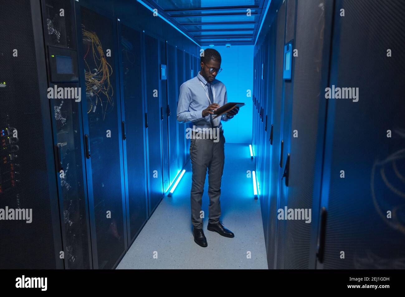 Portrait complet d'un homme afro-américain debout près d'une armoire de serveur tout en travaillant avec un superordinateur dans un centre de données et en tenant une tablette, un espace de copie Banque D'Images