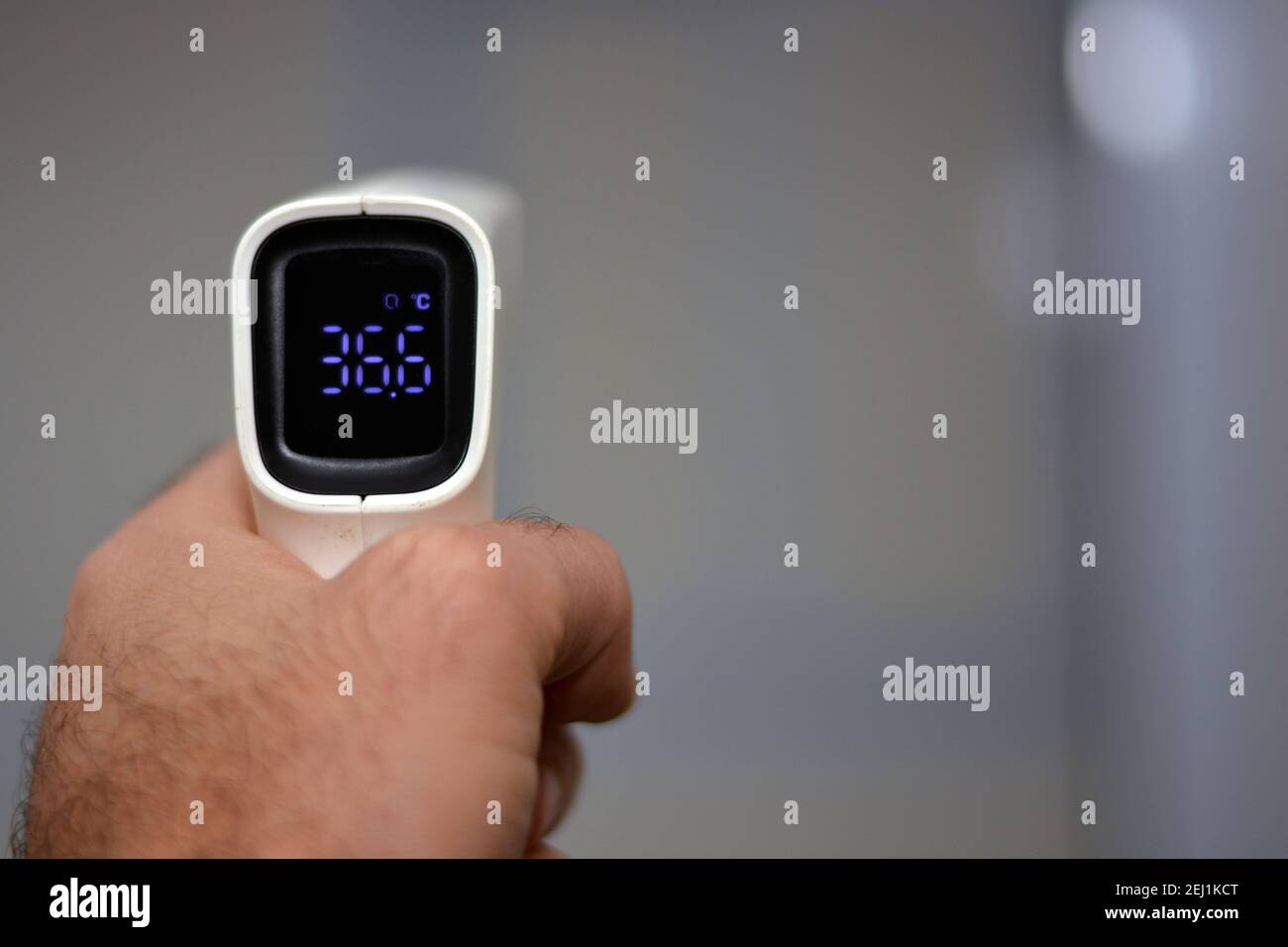 Thermomètre numérique infrarouge frontal sans contact tenu par un jeune homme avec la main gauche et un fond défoqué. Vue rapprochée Banque D'Images