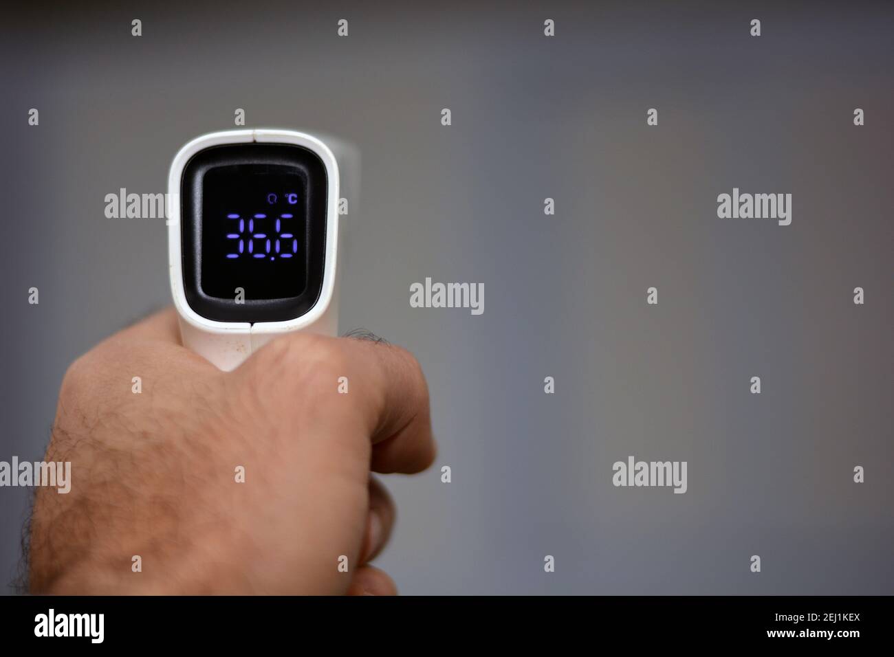 Thermomètre numérique infrarouge frontal sans contact tenu par un jeune homme avec la main gauche et un fond défoqué. Vue rapprochée Banque D'Images