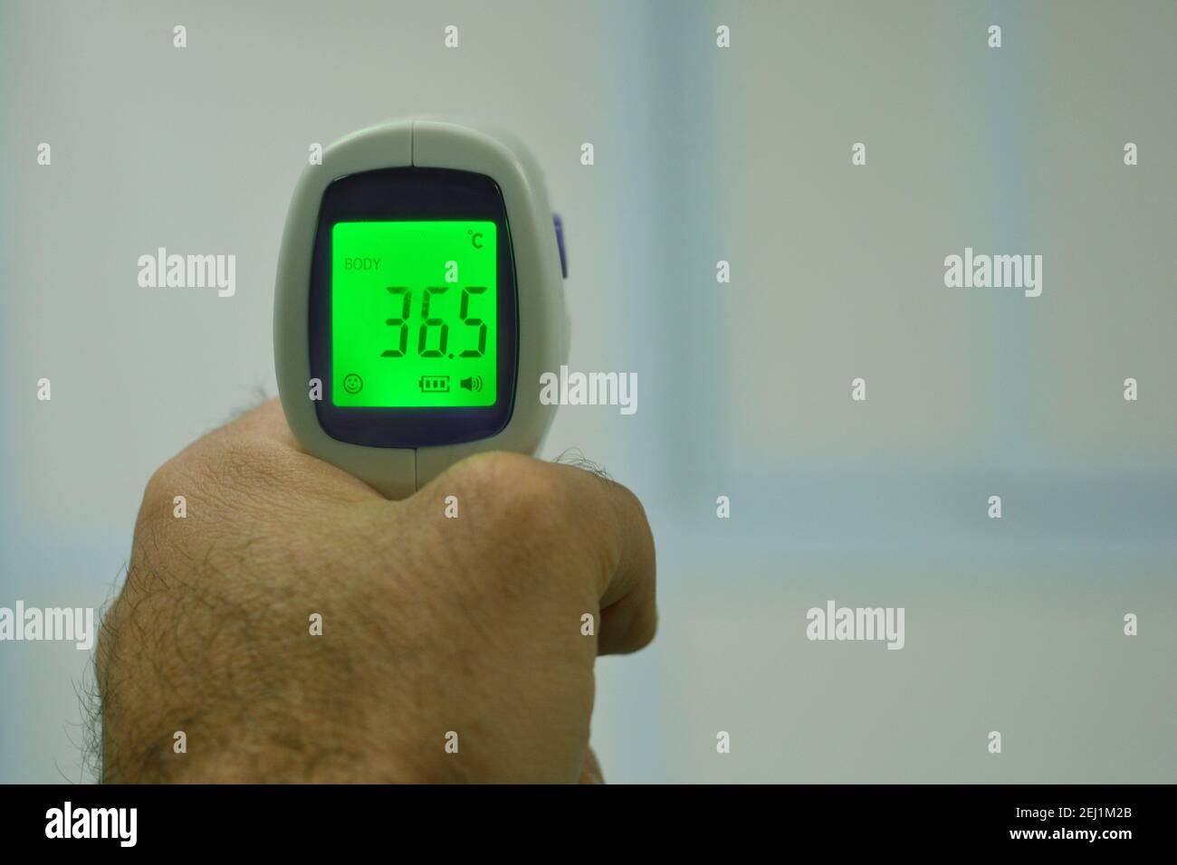 Thermomètre numérique infrarouge frontal sans contact tenu par un jeune homme avec la main gauche et un fond défoqué. Vue rapprochée Banque D'Images