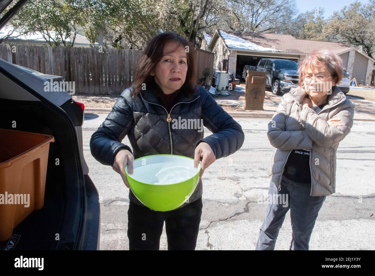 Austin, Texas États-Unis 20 février 2021 : Hank Lam, propriétaire d'une maison, porte un pot d'eau de l'arrière du SUV d'un ami en direction de sa maison lors d'une urgence aquatique dans le centre du Texas. Des températures exceptionnellement basses ont provoqué des tuyaux d'eau gelés et cassés dans toute la région, laissant les résidents sans eau courante et les envoyant s'éparpiller pour l'eau potable. Crédit : Bob Daemmrich/Alay Live News Banque D'Images