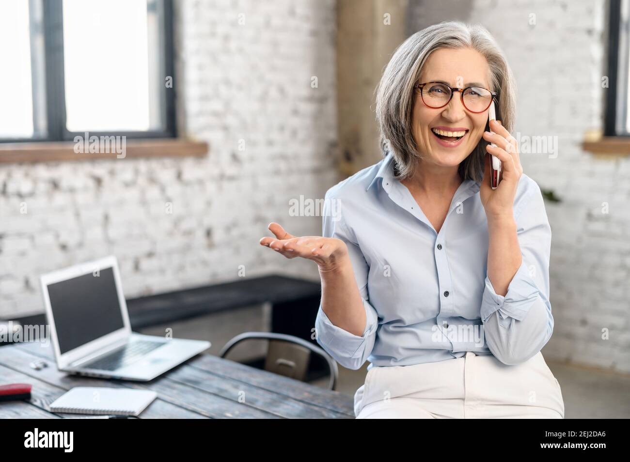Femme d'affaires moderne et excitée Manager en lunettes et tenue décontractée debout dans le bureau, prendre une pause pour appeler et parler à la famille, tenant Banque D'Images
