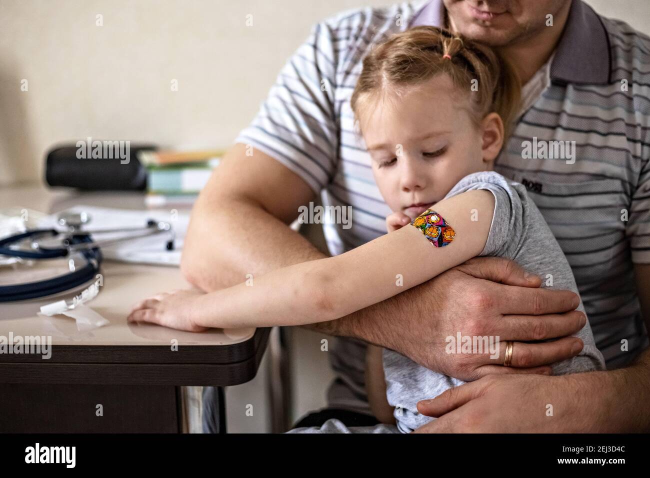 Vaccination d'une petite fille dans les bras de son père dans le bureau du médecin à partir du coronavirus. Plâtre adhésif amusant pour enfants. Vaccin contre le covid-1 Banque D'Images