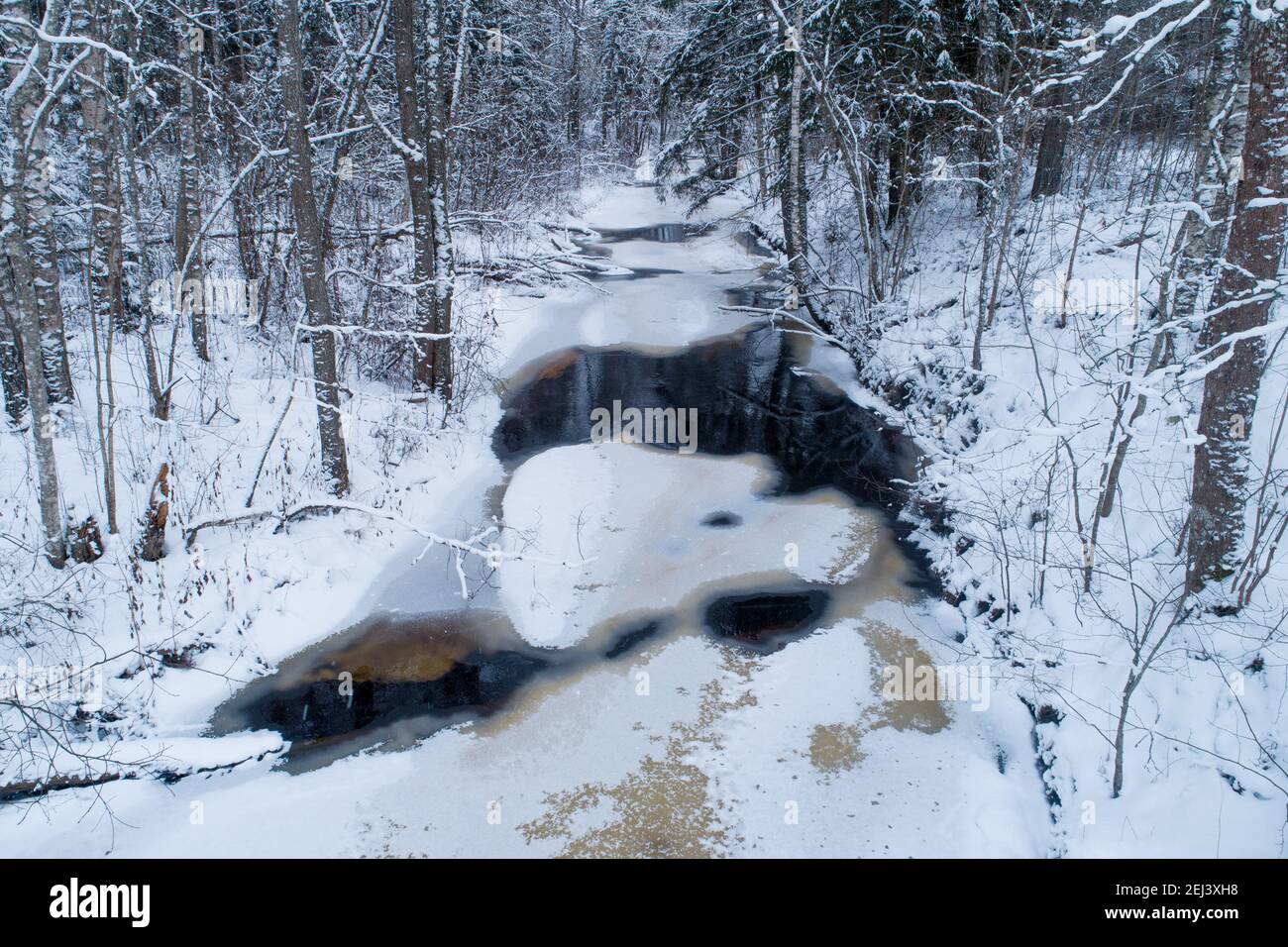 Une petite rivière gèle pendant un hiver froid et enneigé en Estonie, en Europe du Nord. Banque D'Images