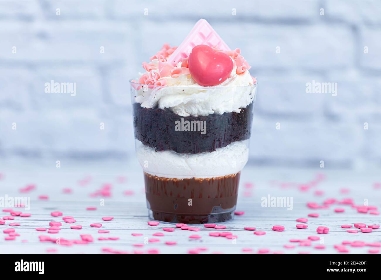 Dessert sucré au chocolat brun et à la crème blanche aérée dans un verre transparent. Le gâteau est décoré de chocolat rose et d'un coeur maurique. Anniversaire Banque D'Images