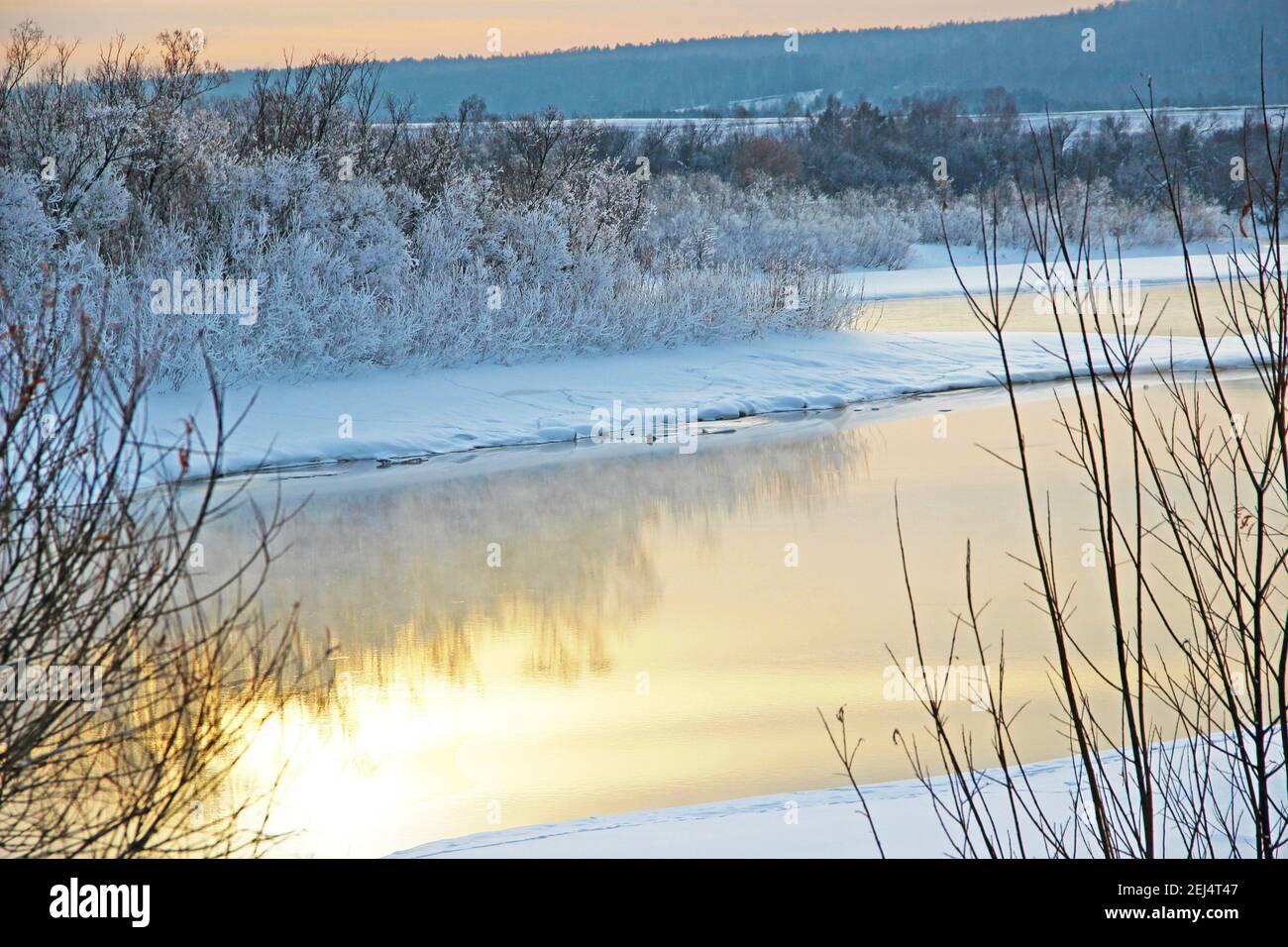 La rivière d'hiver s'étend entre les rives enneigées et le reflet du ciel crée juste un paysage fantastique. Banque D'Images