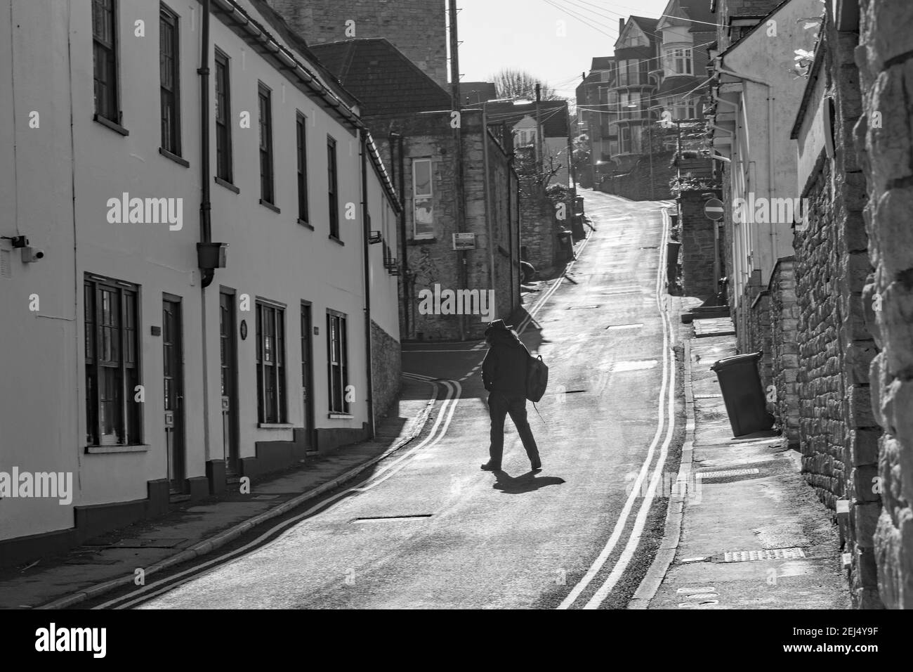 un piéton traverse la rue pavée escarpée vide en silhouette Porter un chapeau comme le Cowboy Midstride Banque D'Images