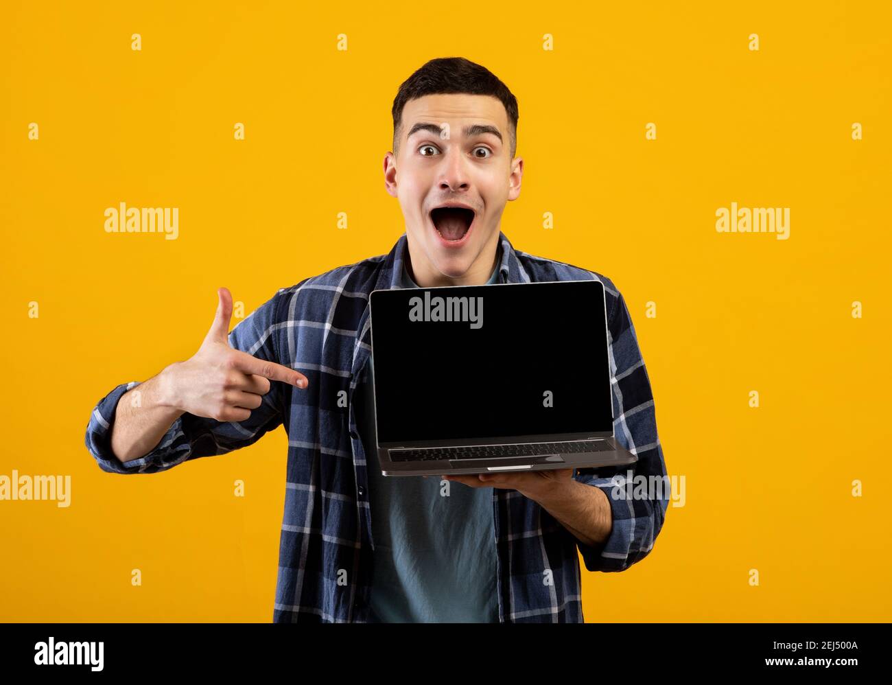 Un homme caucasien excité pointant sur un écran d'ordinateur portable vide avec maquette pour la conception de sites web sur fond orange studio Banque D'Images
