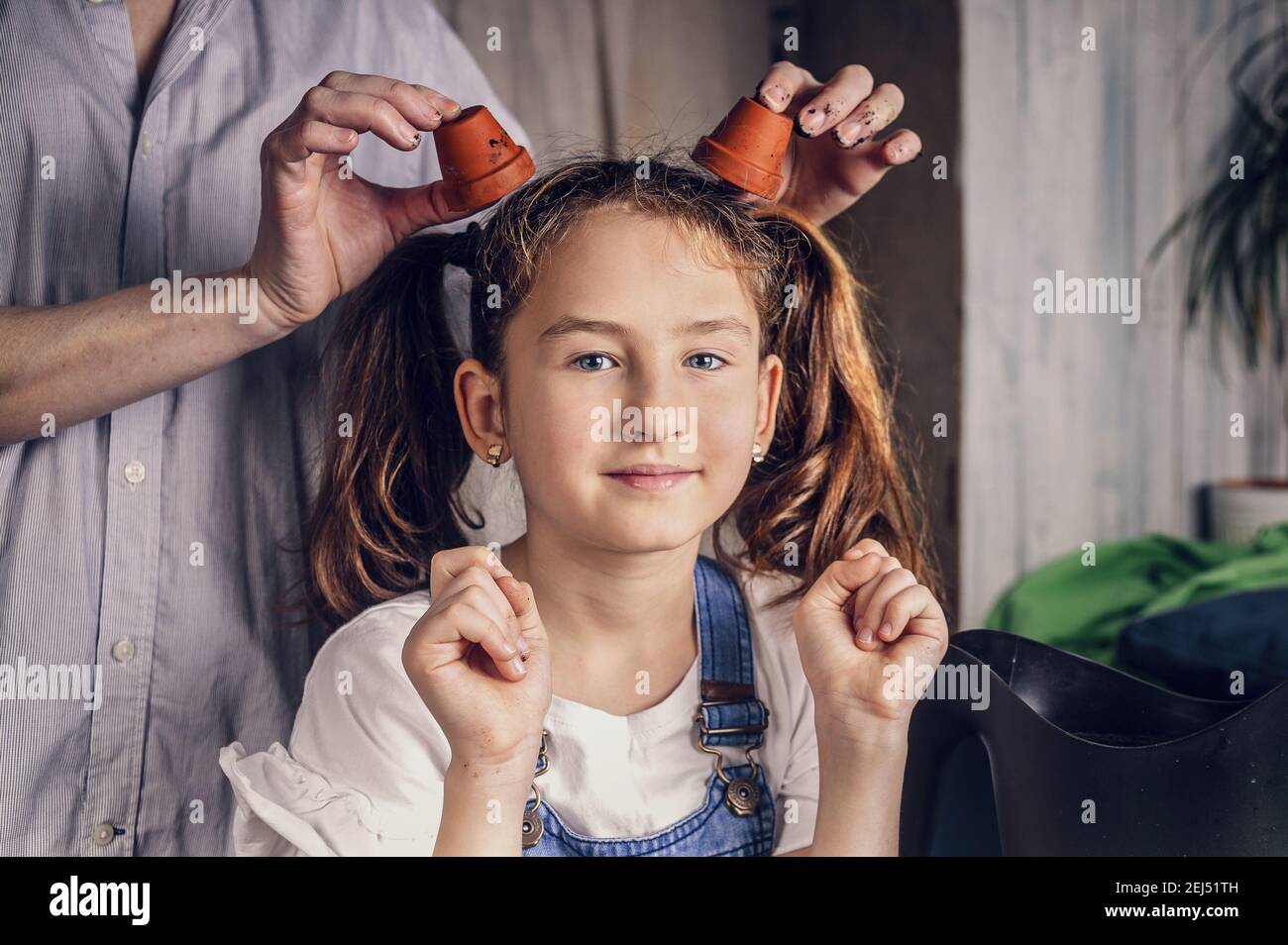 joyeuse belle fille joue avec des pots de fleurs avec sa mère pendant le jardinage à la maison. enfance heureuse, activité familiale intérieure. ethnie caucasienne Banque D'Images