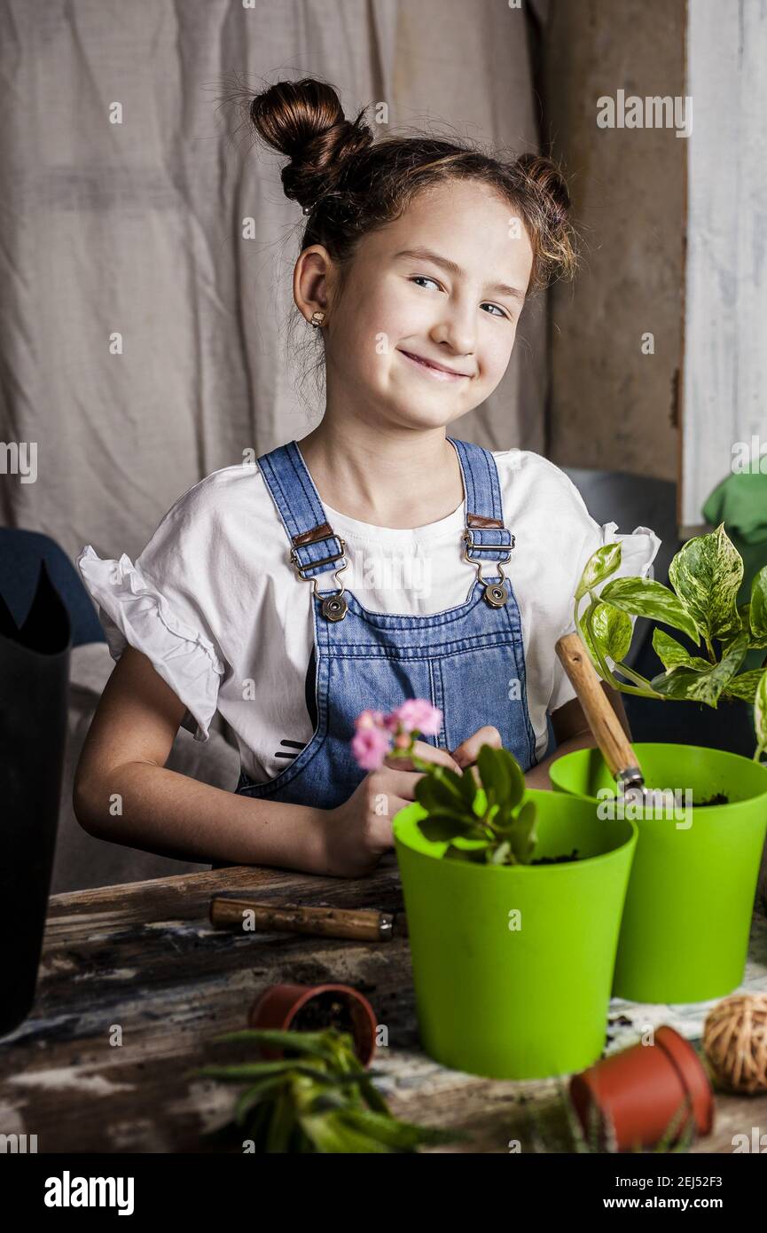 jolie fille souriante avec des cheveux plante une plantule dans un pot de fleurs. activité de printemps à l'intérieur. ethnie caucasienne. vue de face. photo verticale. Banque D'Images