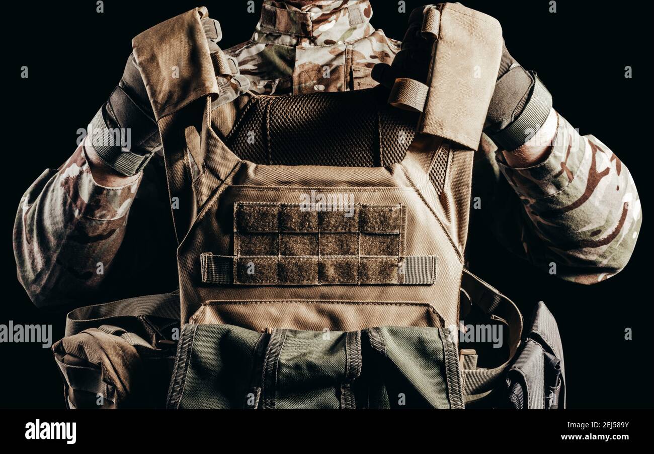 Photo d'un soldat en uniforme de camouflage et gants tactiques tenant une veste blindée militaire sur fond noir. Banque D'Images