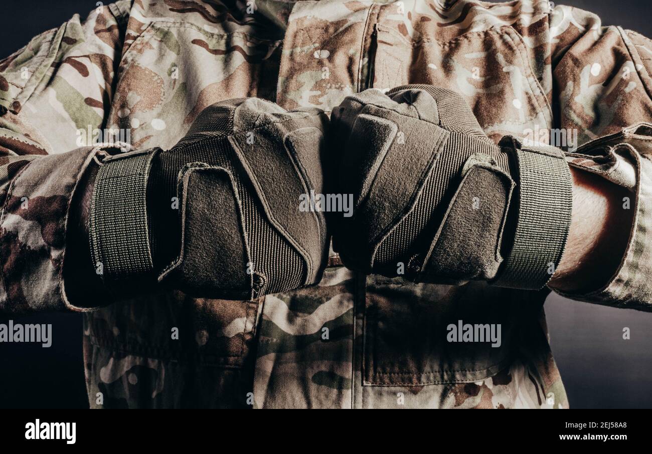 Photo d'un soldat en uniforme camouflé montrant le geste de combat du poing dans des gants tactiques sur fond noir. Banque D'Images