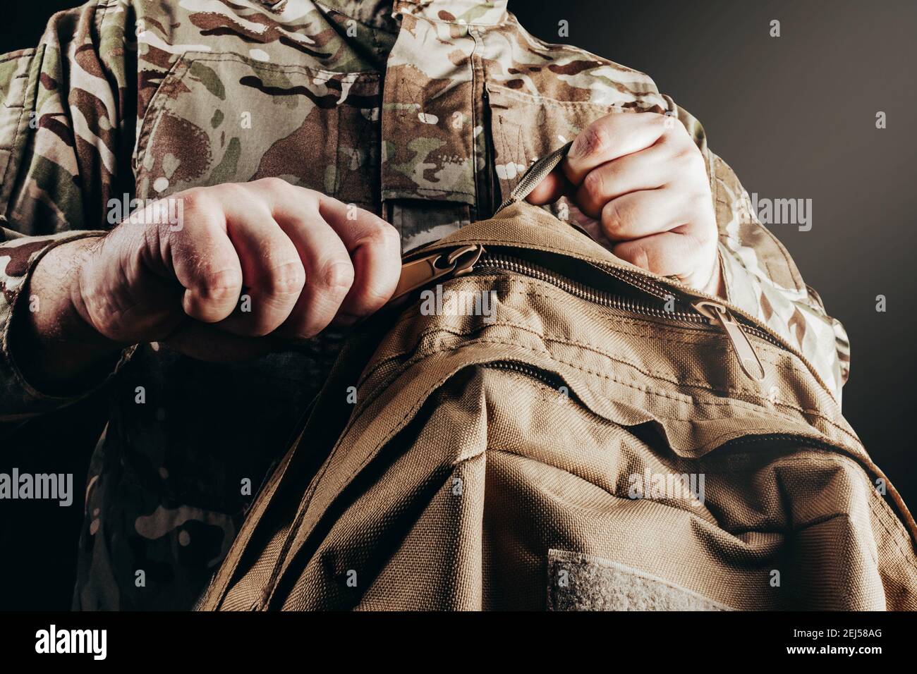 Photo d'un soldat dans un uniforme de camouflage et sac à dos à dézipper sur fond noir. Banque D'Images