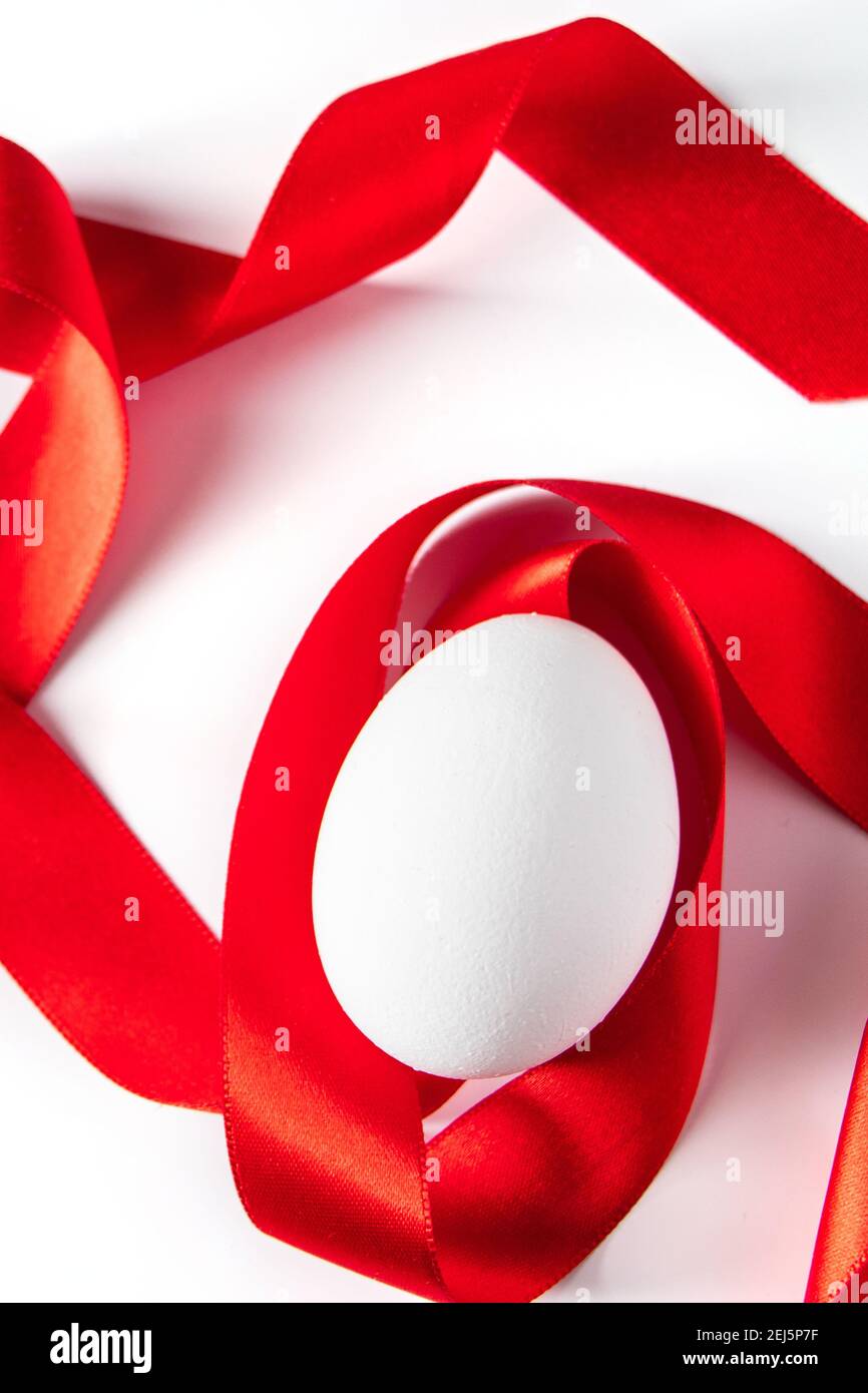 Gros plan œuf blanc avec ruban de soie rouge, symbole pâques sur fond clair. Placer pour le texte. Banque D'Images