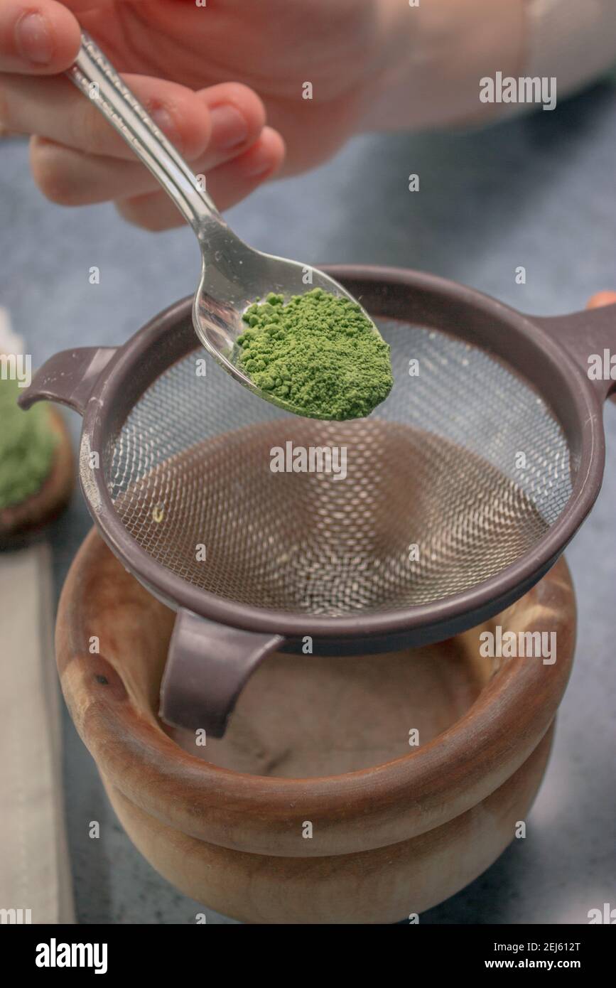 Image verticale de la poudre de thé matcha avec la passoire à saupoudrer dans un bol en bois sur fond de pierre grise. Thé vert japonais. Préparation du thé Matcha 2021. Banque D'Images