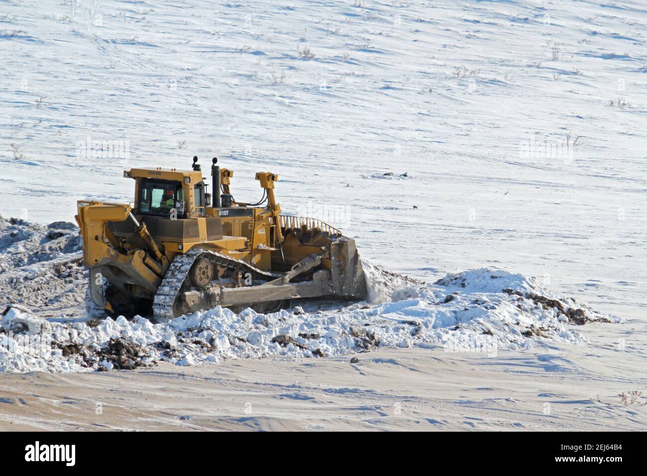 Bulldozer Caterpillar poussant la neige pendant la construction hivernale de la route Inuvik-Tuktoyaktuk, Territoires du Nord-Ouest, Arctique canadien. Banque D'Images