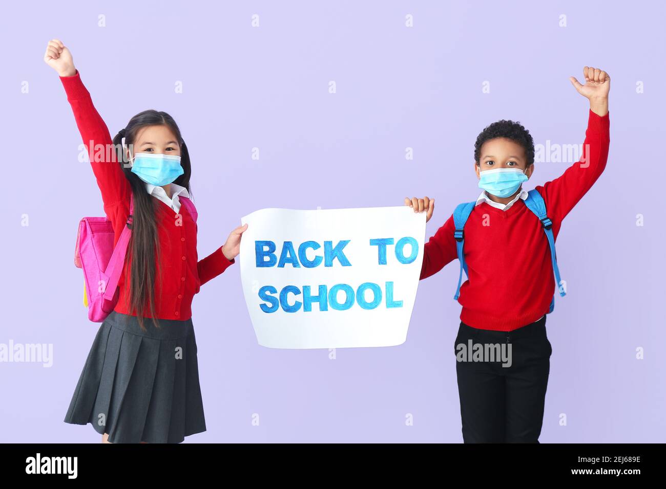 Petits enfants dans des masques médicaux tenant l'étiquette avec le texte DE RETOUR À L'ÉCOLE sur fond de couleur. Épidémie de coronavirus Banque D'Images