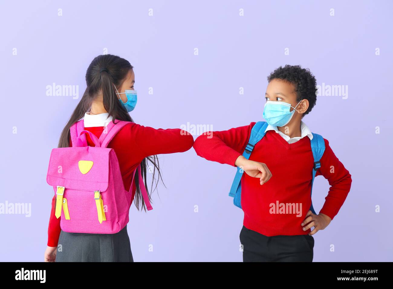 Les petits écoliers se saluant dans des masques médicaux sur fond de couleur. Épidémie de coronavirus Banque D'Images