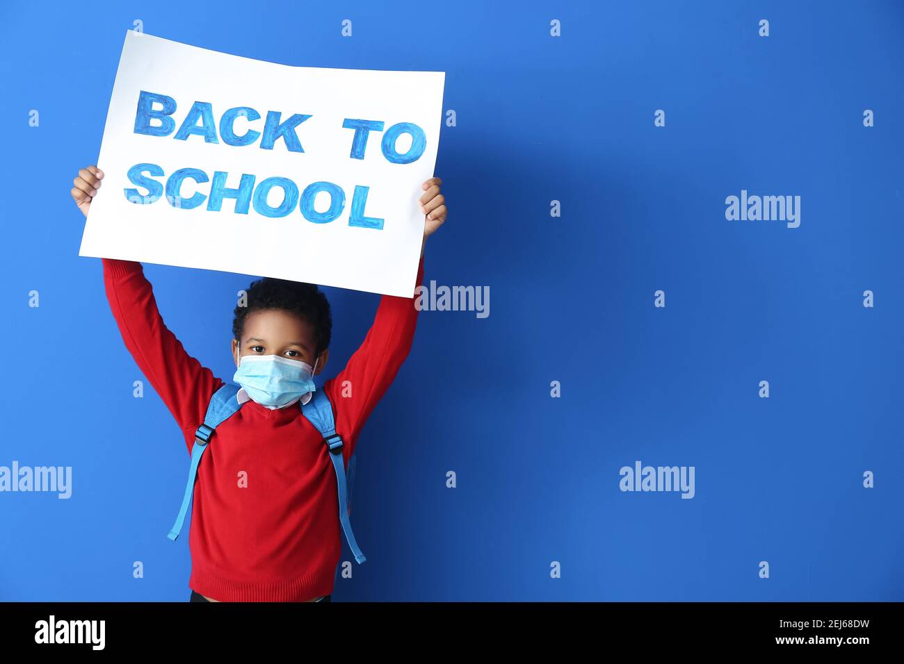 Petit garçon afro-américain dans un masque médical portant un écriteau avec texte DE RETOUR À L'ÉCOLE sur fond de couleur. Épidémie de coronavirus Banque D'Images