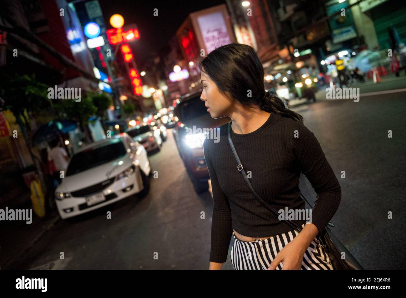 Jeune fille d'Asie belle dans une rue très fréquentée la nuit, marchant tout en regardant en arrière par-dessus son épaule. Feux de la ville et circulation en arrière-plan. Banque D'Images