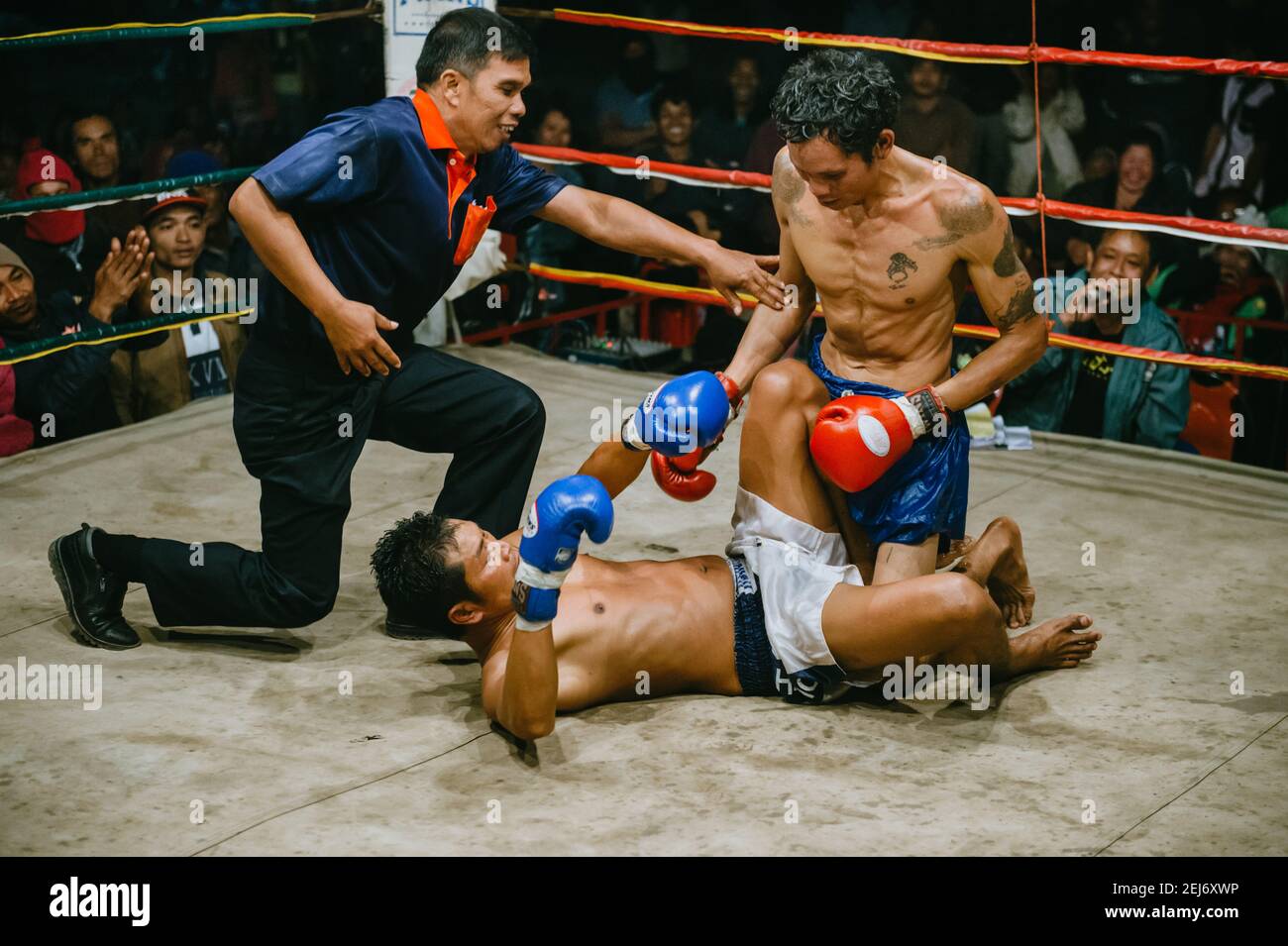 Muay Thai combat dans l'isan, la Thaïlande rurale, la boxe thaï, l'arbitre essayant d'empêcher le boxeur de poinçonner l'adversaire couché sur le sol. Banque D'Images