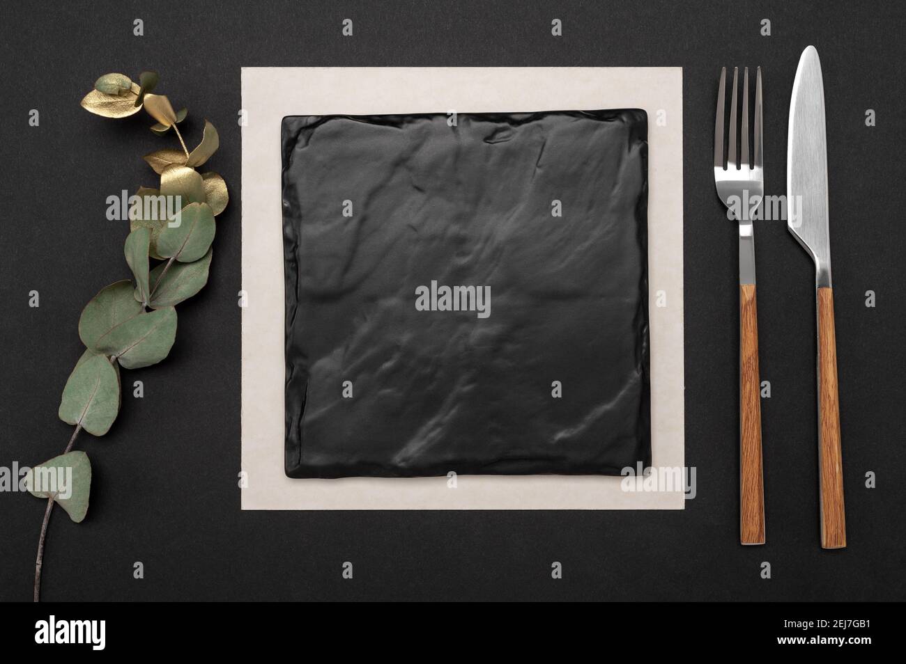 Couteau et fourchette avec plaque carrée en ardoise noire pour le texte du menu ou de la recette et branche d'eucalyptus d'or sur table noire. Maquette planche vierge et couverts sur le bac Banque D'Images Couteau et fourchette avec plaque carrée en ardoise noire pour le texte du menu ou de la recette et branche d'eucalyptus d'or sur table noire. Maquette planche vierge et couverts sur le bac Banque D'Images