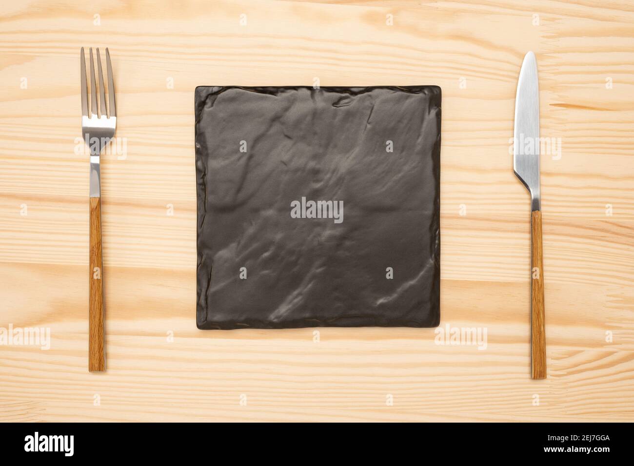 Couteau et fourchette avec plaque carrée en ardoise noire pour le texte du menu ou de la recette sur une table noire. Maquette planche vierge et couverts sur fond de table rustique en bois Banque D'Images