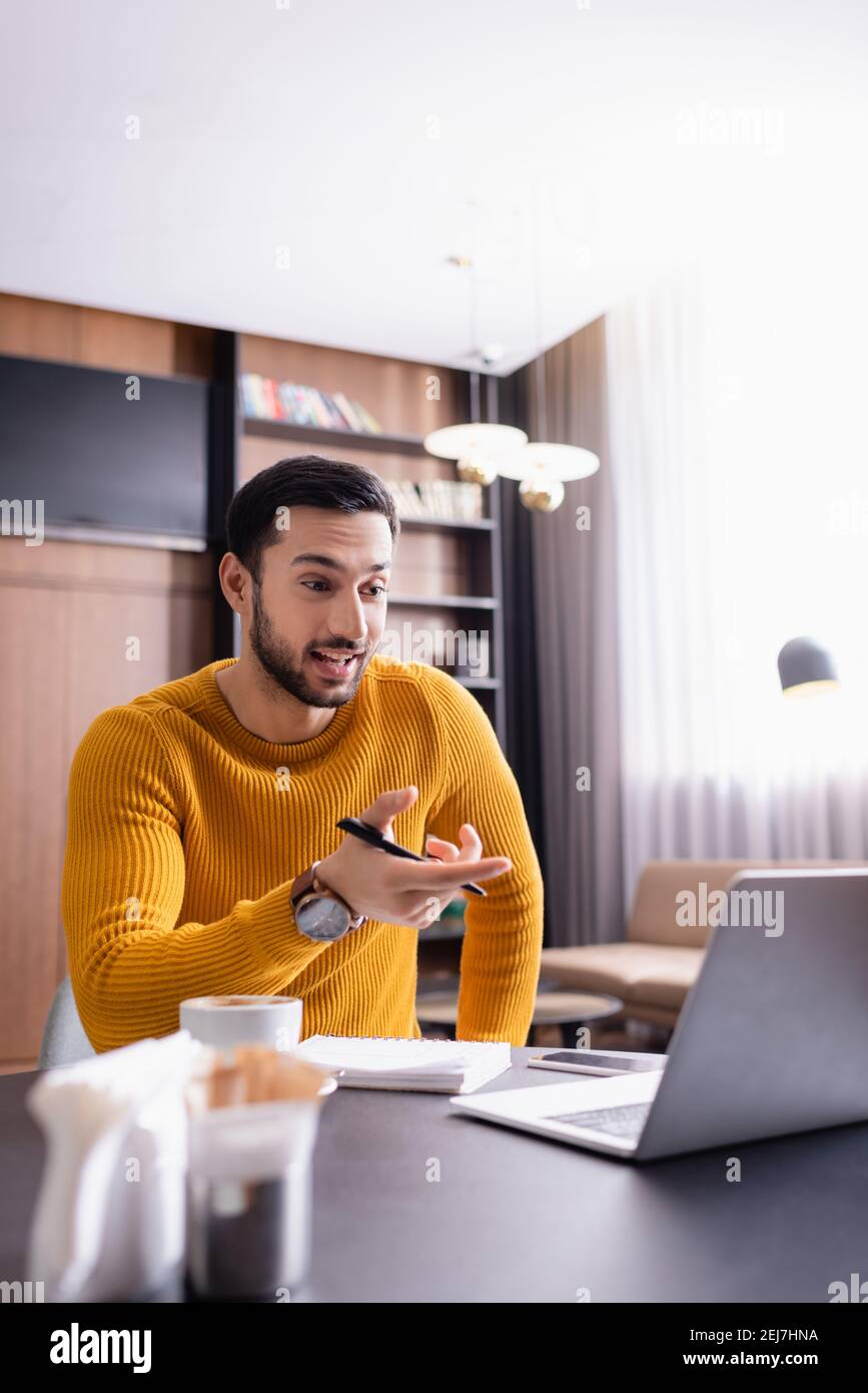 un pigiste arabe étonnant pointant vers un ordinateur portable dans un restaurant, avant-plan flou Banque D'Images