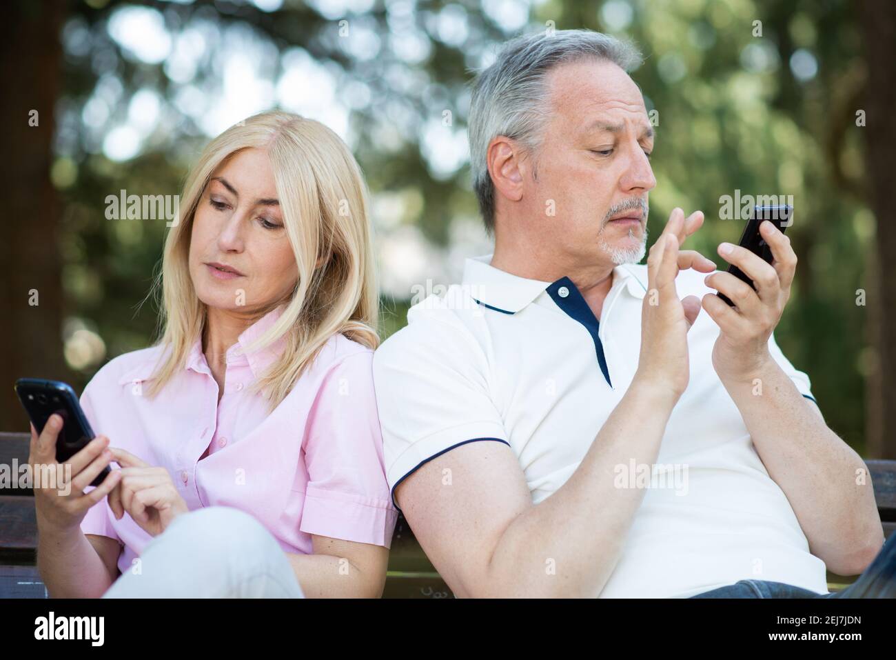 Triste couple utilisant leur propre smartphone pendant qu'il est dans un parc, smartphone addiction et couple problèmes concept Banque D'Images