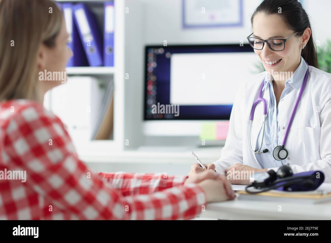 Femme médecin écrivant dans les antécédents médicaux et parlant avec le patient Banque D'Images