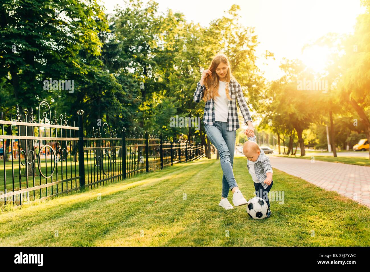 Une jeune maman heureuse et son petit fils jouent au football ensemble plein air dans le parc Banque D'Images