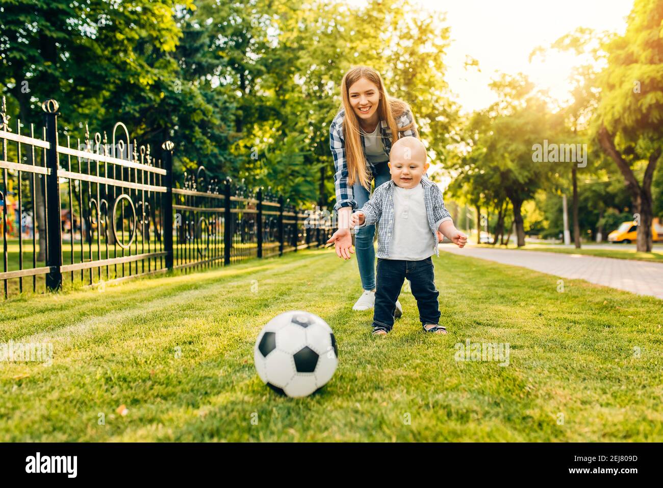 Une jeune maman heureuse et son petit fils jouent au football ensemble plein air dans le parc Banque D'Images