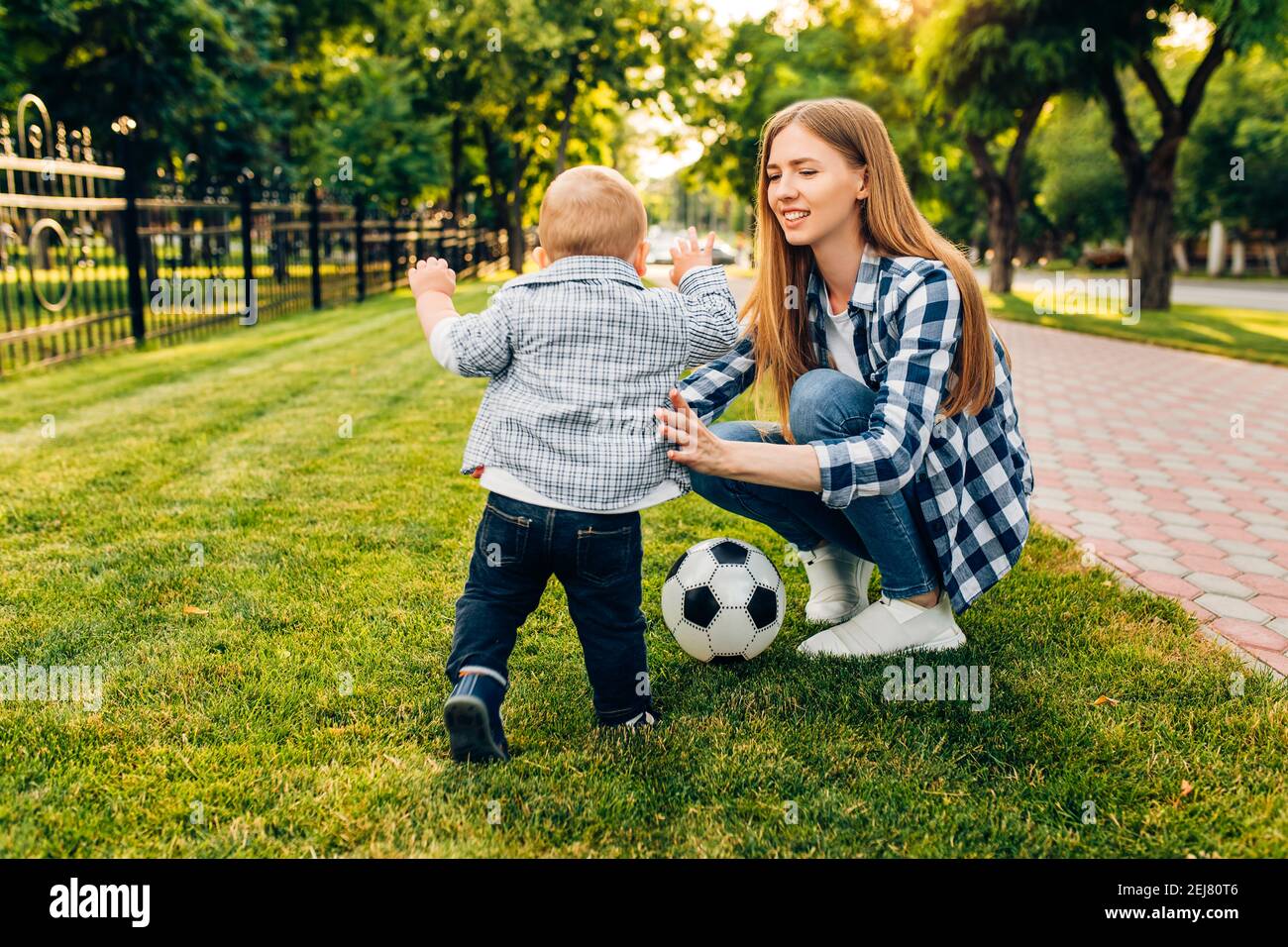 Une jeune maman heureuse et son petit fils jouent au football ensemble plein air dans le parc Banque D'Images