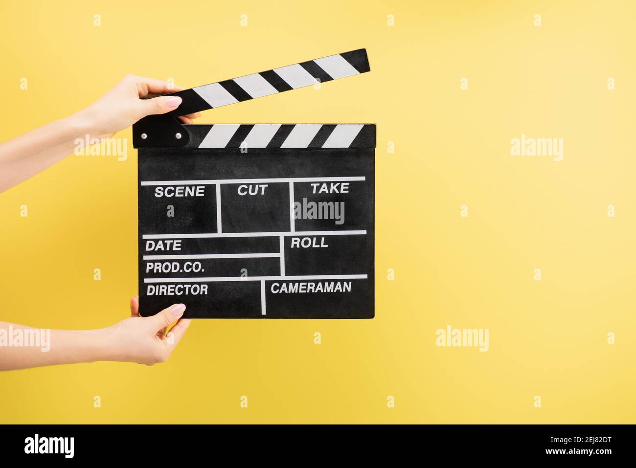 vue partielle de l'assistant de caméra tenant le clapperboard isolé sur jaune, concept de cinéma Banque D'Images