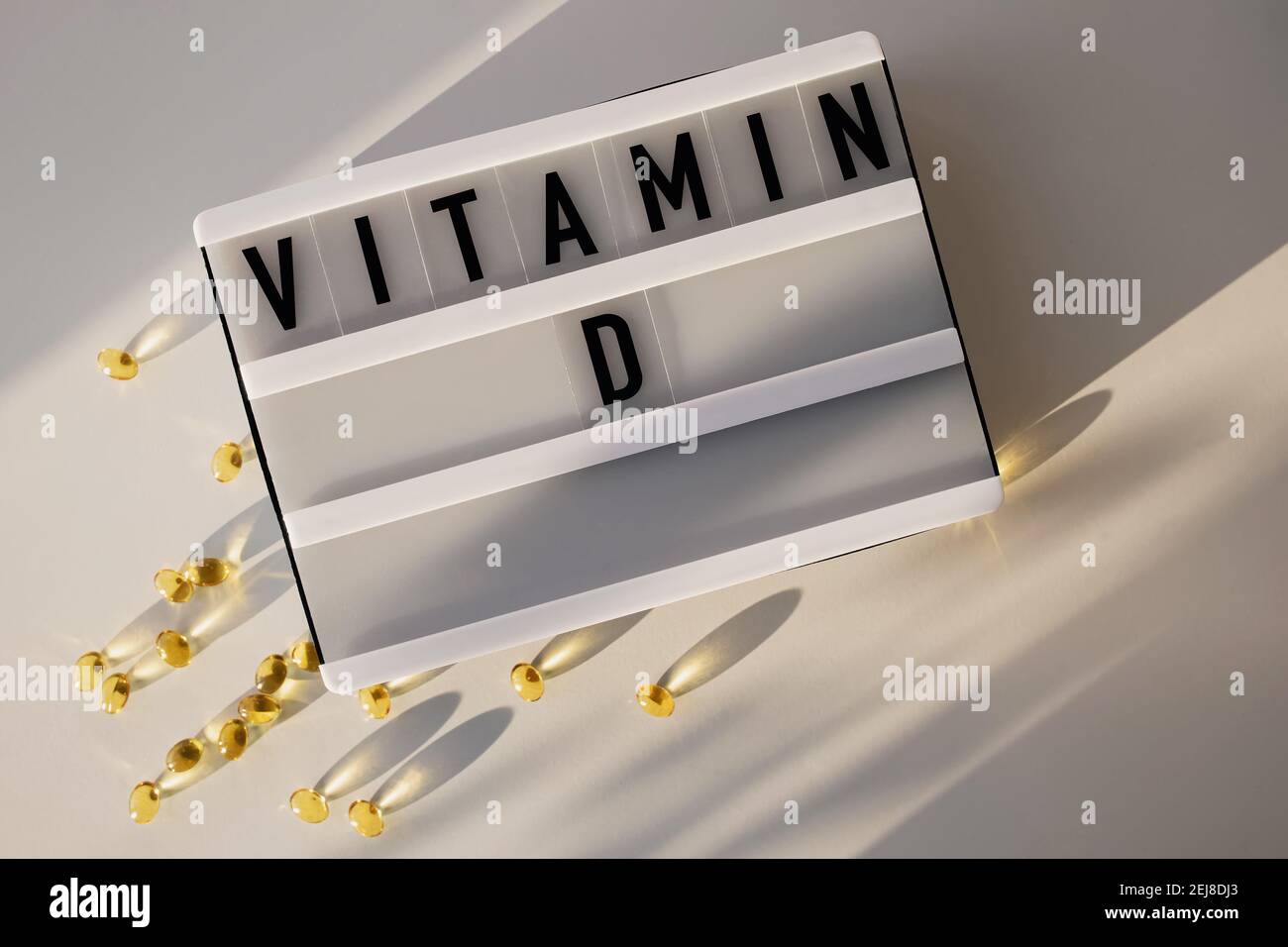 Capsules de vitamine D sur la table blanche avec lumière naturelle du soleil. Banque D'Images