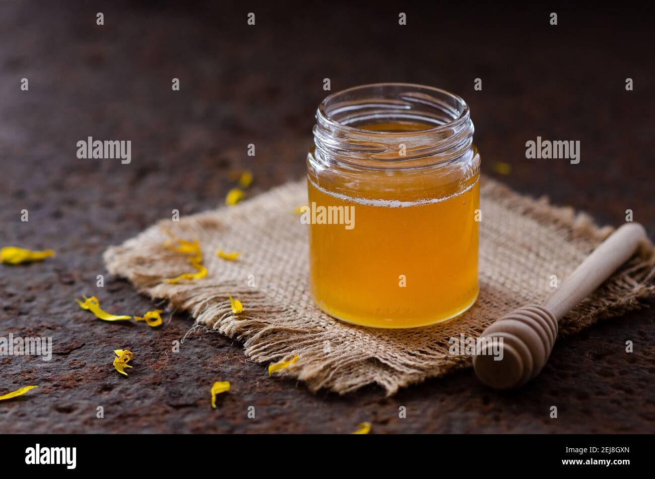 Miel dans un bocal aux pétales de pâquerette jaune et un bol de miel. Banque D'Images