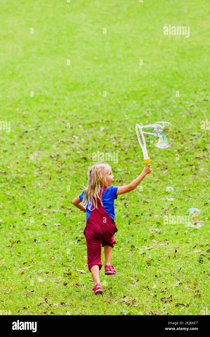Bonne fille jouant avec des bulles de savon. Enfant actif courir dans le parc . Style de vie en famille, activités de plein-temps, vacances d'été avec les enfants. Banque D'Images