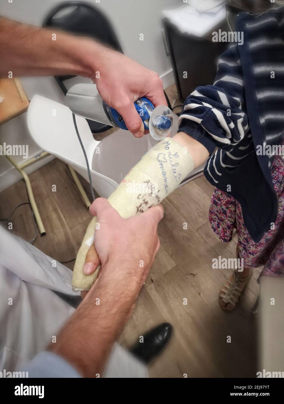 Medecin coupant le plat avec une machine vibrante à une fillette Européenne de 8 ans au poignet fracturé il y a 6 semaines, France. Banque D'Images