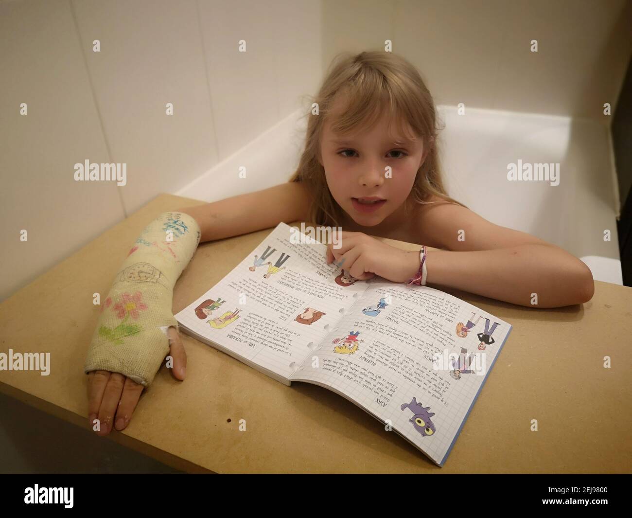 Portrait d'une fillette de 8 ans Européenne au poignet cassé, plateau, lisant sur une nappe en bois un exercice dans son bain , France. Banque D'Images