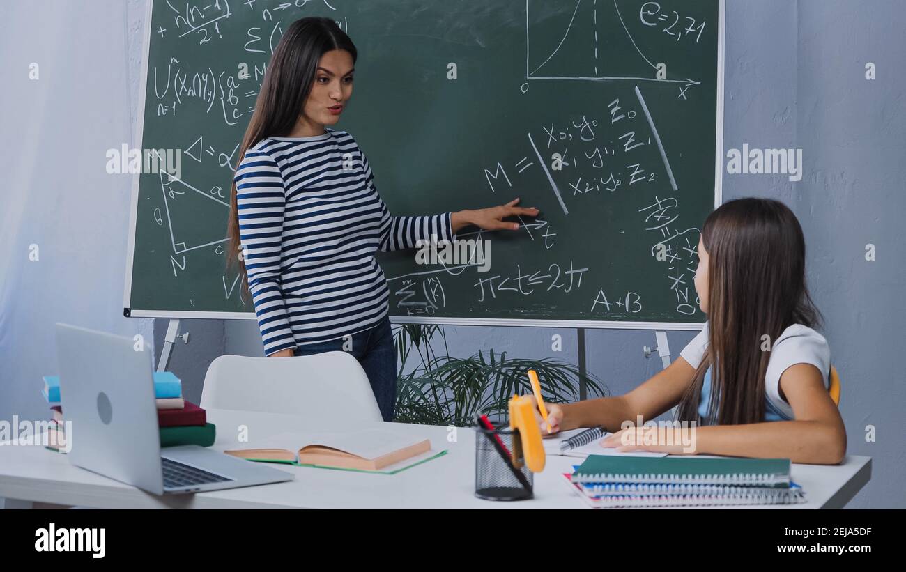 mère pointant avec la main au tableau noir avec des formules mathématiques près fille Banque D'Images