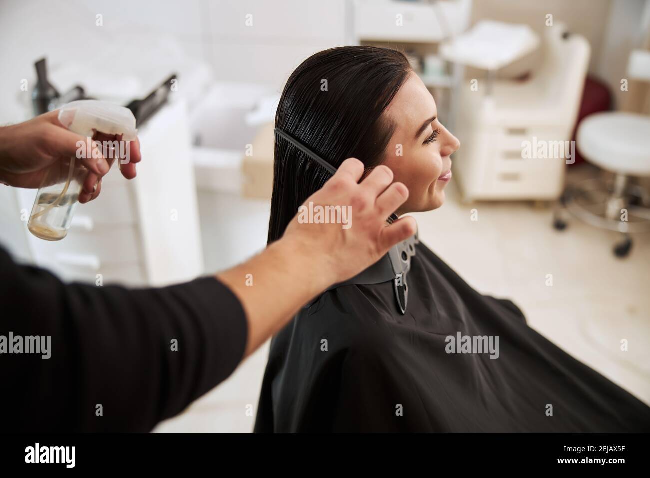 Coiffeur professionnel lissant les cheveux souriants de la femme Banque D'Images